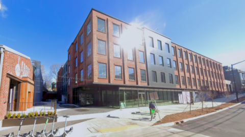 An image showing a large brick and glass building over a wide street with wide open interiors.