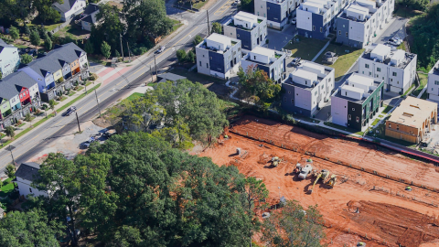 An image of a large townhome development next to wide street on red clay earth in eastside Atlanta, next to many trees and new townhomes.