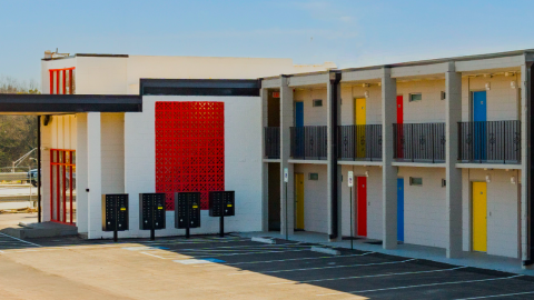 A photo of a two-story white hotel with many colorful doors in red blue and yellow with white walls and white interiors under a blue sky near wide streets and interstates near downtown Atlanta.