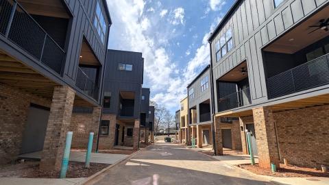 A photo of brick and black duplexes on a corner lot in Atlanta under blue skies near wide roads.