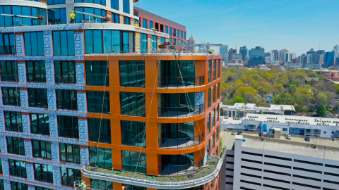 An aerial drone photo of a large new copper-like tower standing over trees and building under blue skies in Atlanta with many balconies.