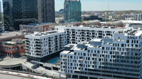 A photo of a large white new stair-stepped apartment complex in Atlanta near many tall buildings and a huge freeway. 