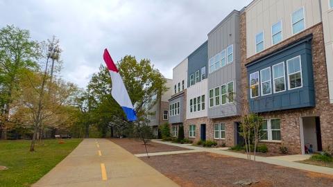 A photo of a stack of modern-style townhomes overlooking a wide pathway next to many trees under gray skies outside Atlanta, with white modern interiors.